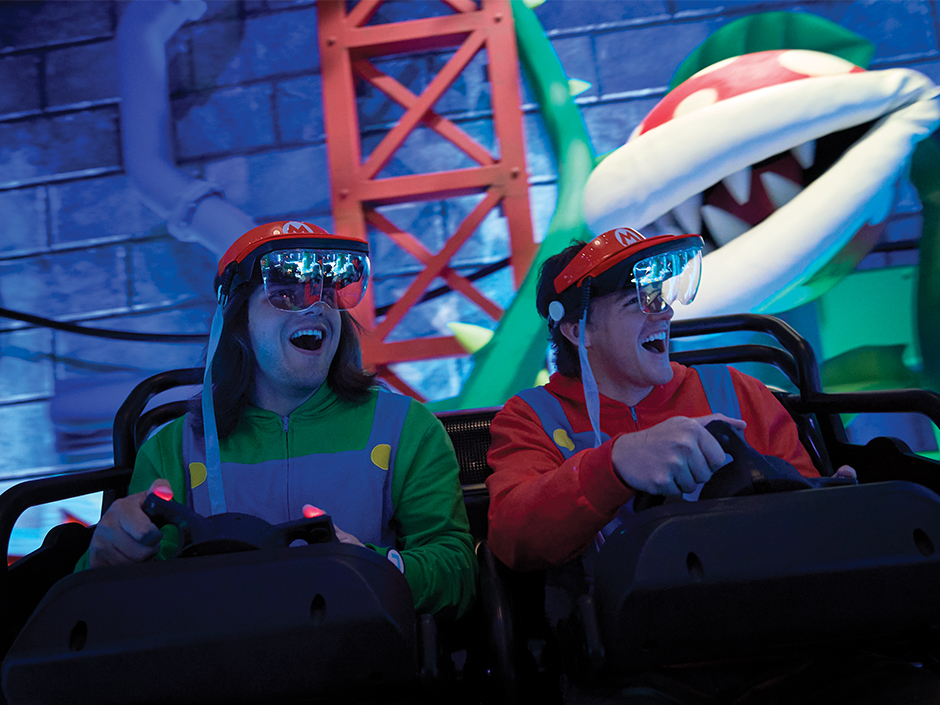 Two boys smile as they drive past a Piranha Plant on Mario Kart: Bowser's Challenge at Epic Universe