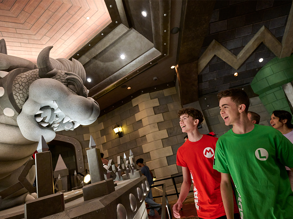 Two young boys in Mario and Luigi shirts marvel at the Bowser statue in the Mario Kart: Bowser's Challenge queue