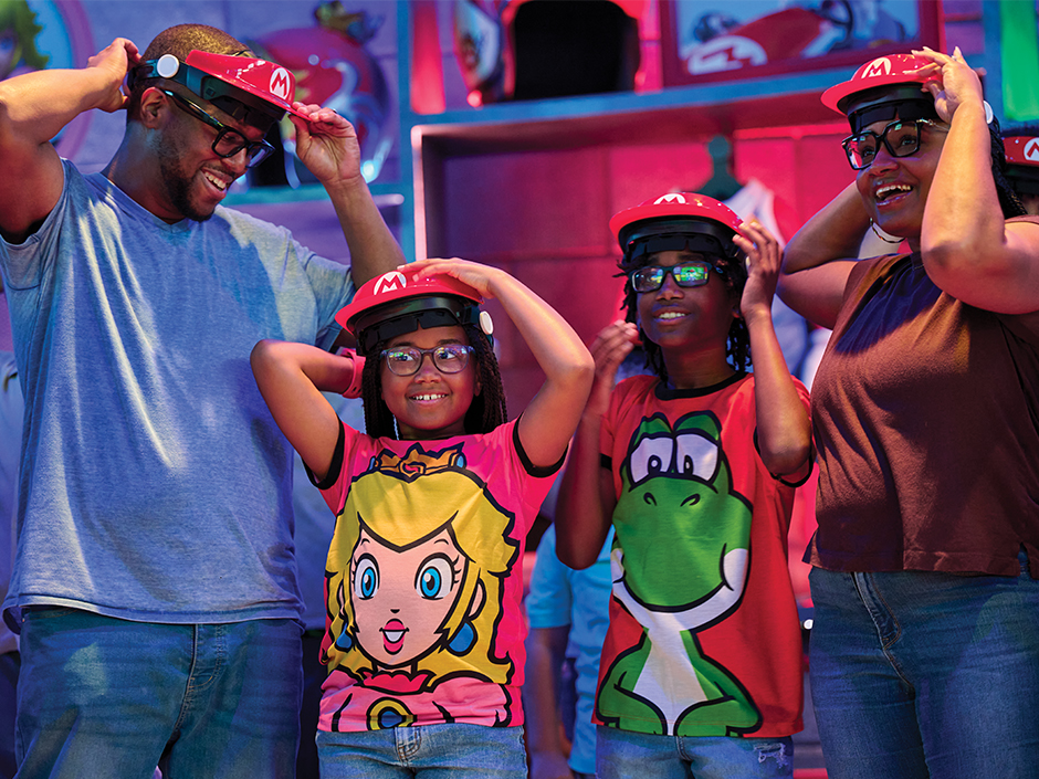 A family of four smiles as they put on their Mario visitors before boarding Mario Kart: Bowser's Challenge