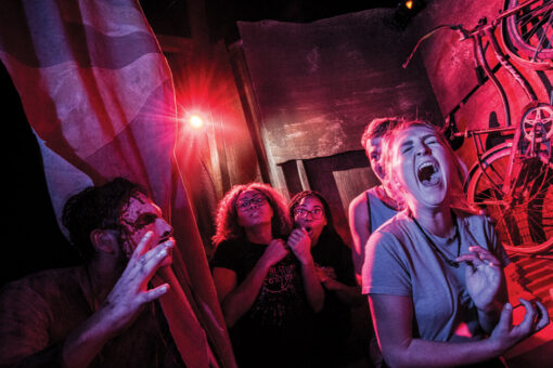 A group of friends scream together as a scare actor jumps out at them in a haunted house at Halloween Horror Nights