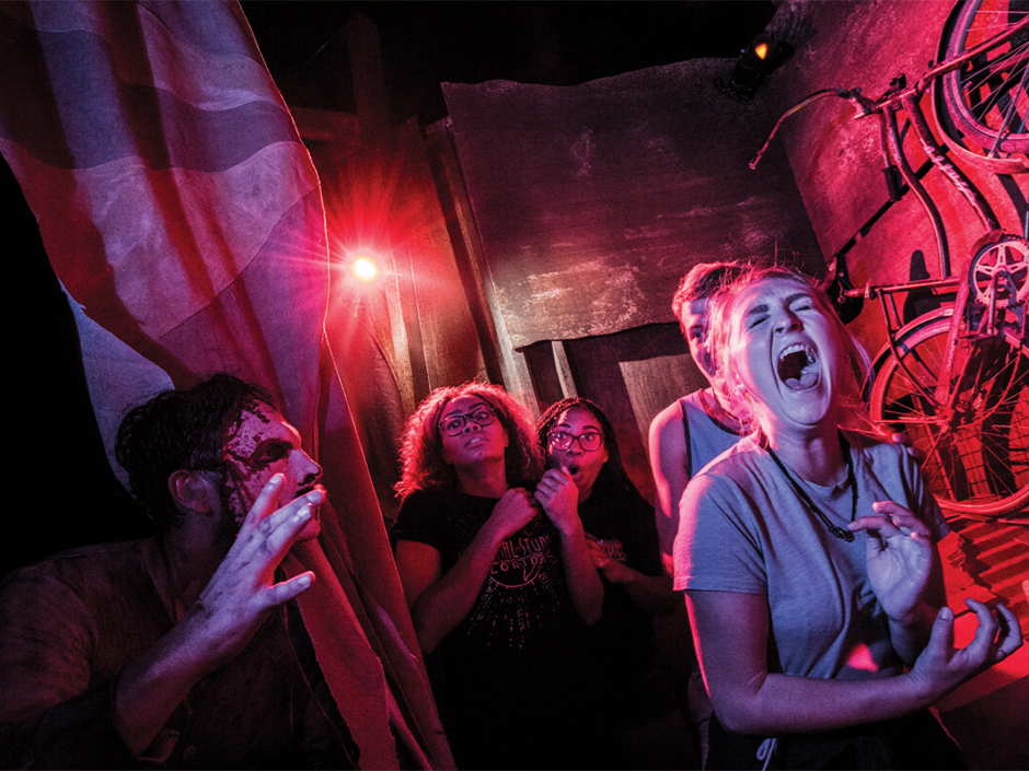 A group of friends scream together as a scare actor jumps out at them in a haunted house at Halloween Horror Nights