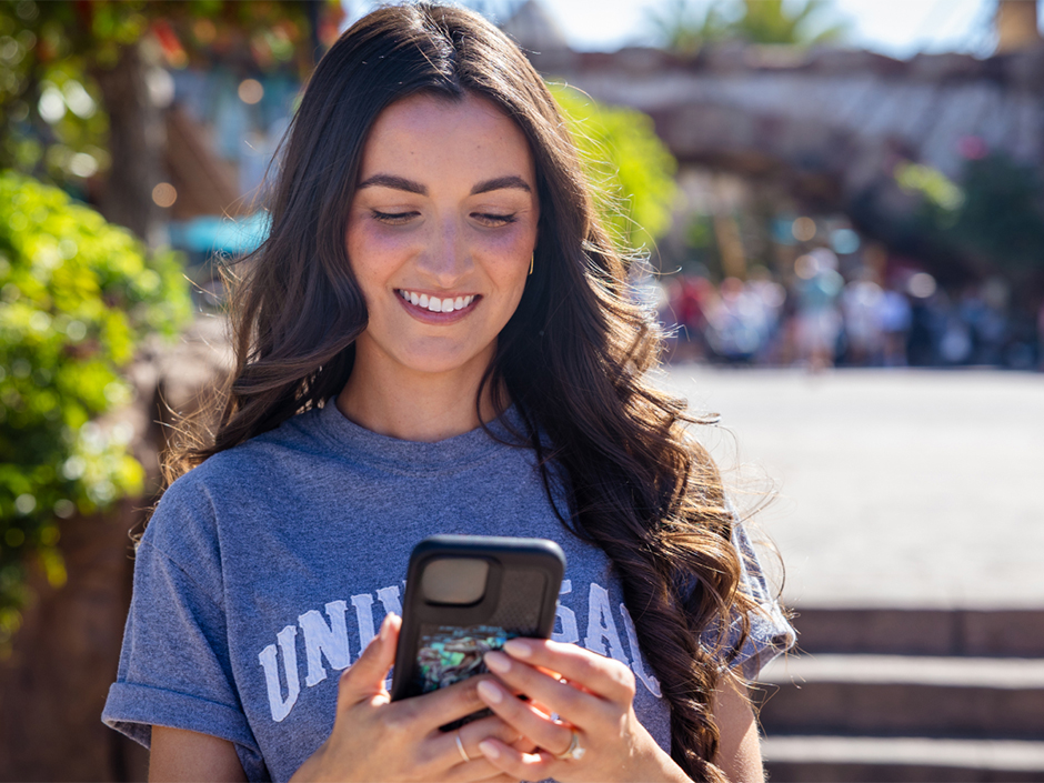A girl smiles at her phone inside Islands of Adventure